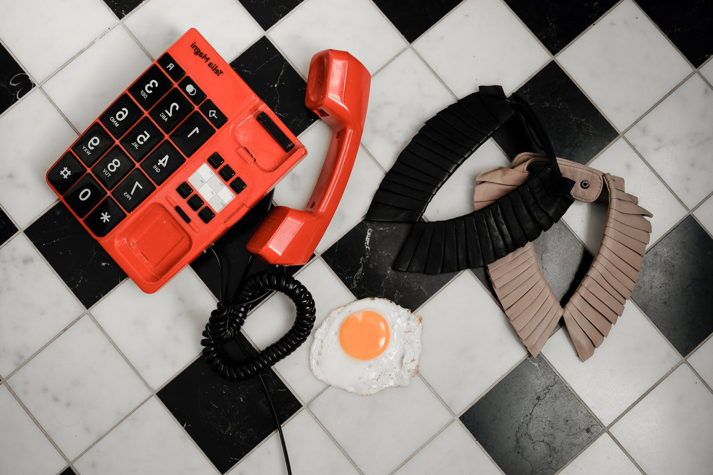 Denduon Mushroom and Black leather collars on checked floor styled with fried egg and retro telephone