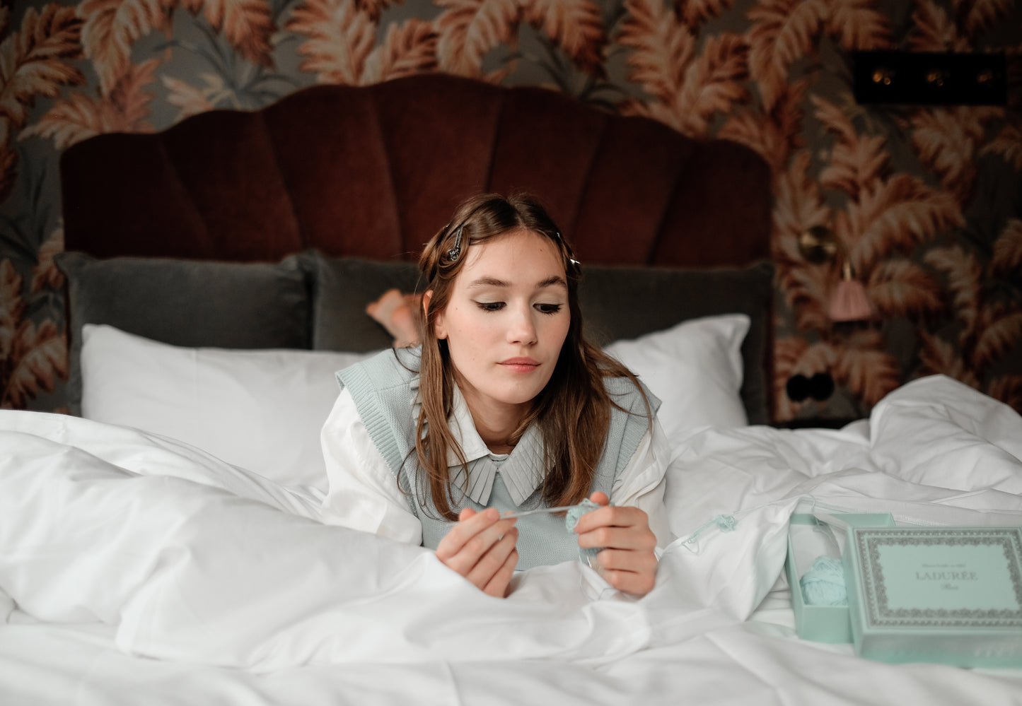 Denduon leather collar meadow mist on woman, laying on hotel bed crotcheting