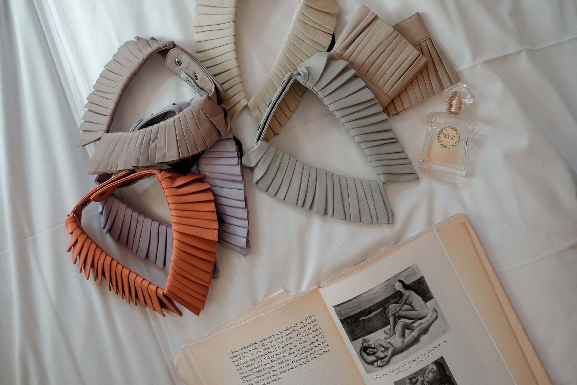 Denduon mixed leathercollars on a bed with book and perfume