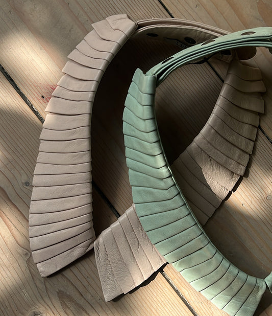Two pleated leather collars in soft pastel leather laying on a wooden floor scandinavian design